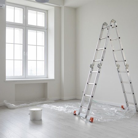 Zimmer während Renovierungsarbeiten mit Leiter, Farbeimer und teils abgedecktem hellgrauen Bodenbelag